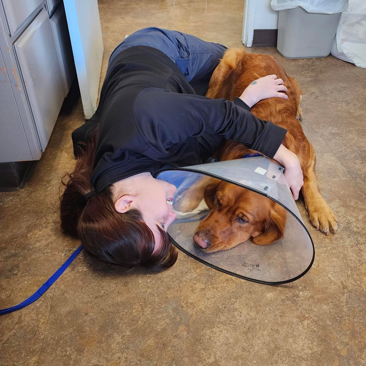 team member laying on floor with dog post-surgery and smiling